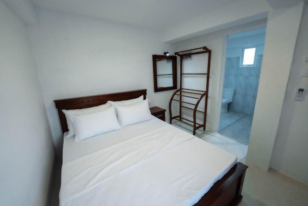 Un dormitorio con una cama, una escalera de madera, una mesita y un baño visible a través de una puerta abierta.