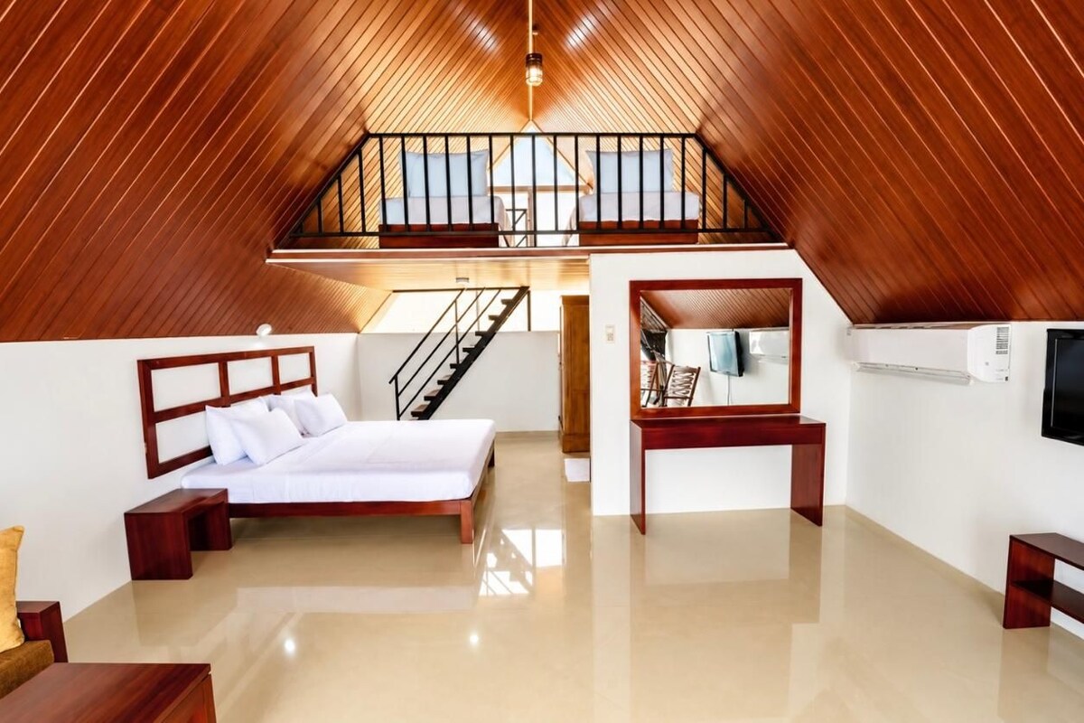 A bedroom with a bed, a desk, a chair, a TV, and a staircase leading to an upper level.