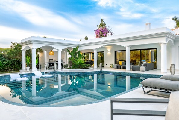 A modern pool area with a clear pool, white columns, and outdoor seating. - Villa 'Beach-side 5B' with Private Pool, Private Terrace and Air Conditioning (El Paraíso)
