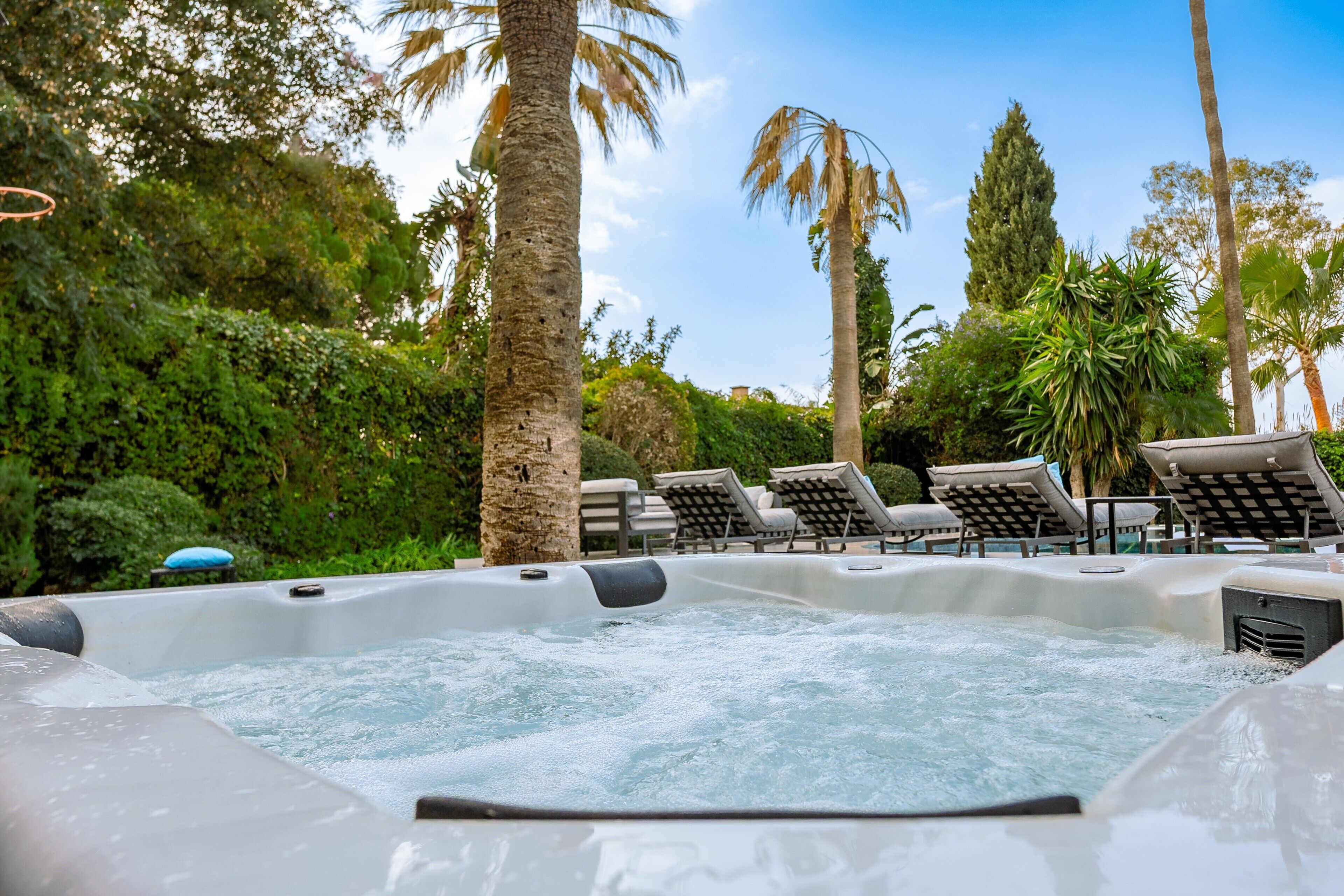 Un bain à remous rempli d’eau, entouré de chaises longues et de palmiers.
