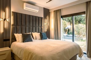 A modern bedroom with a large bed, a built-in headboard, a nightstand, and a window with curtains. - Villa 'Beach-side 5B' with Private Pool, Private Terrace and Air Conditioning (El Paraíso)