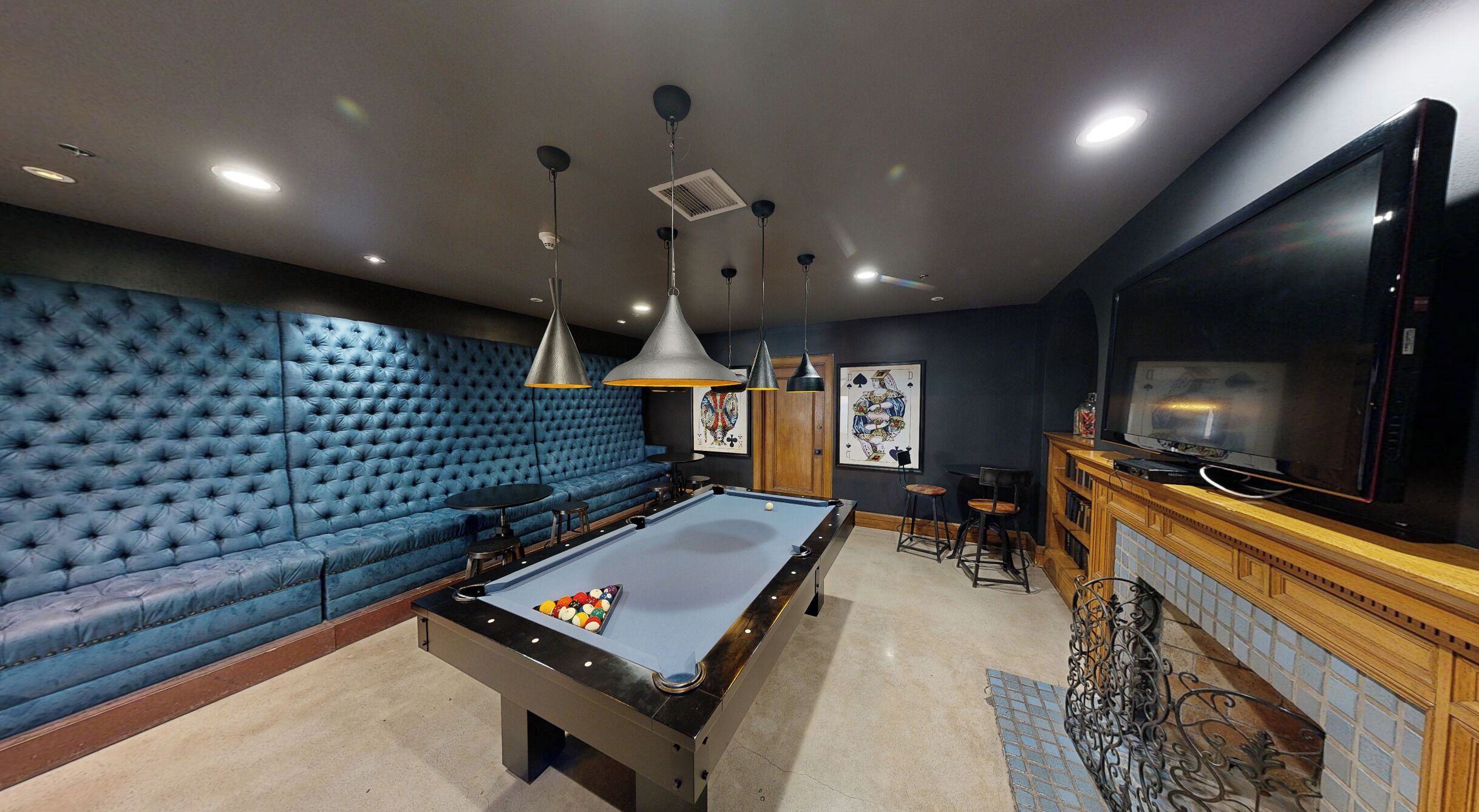 A pool table with a blue felt surface, a blue tufted sofa, and a television on a wooden cabinet.