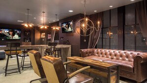 Zona de bar con asientos de cuero, una mesa de madera y una pantalla de televisión mostrando un programa.