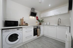 A modern kitchen with white cabinetry, a microwave, an oven, a washing machine, and a sink. - Norfolk House - Steps from Quays, Parks & Docks (Gloucestershire)