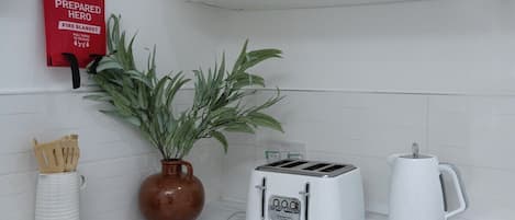 Cocina con encimera blanca, tostadora, hervidor, planta y extintor rojo.