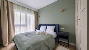 A neatly made bed with rolled towels, a bedside table with a lamp, and a view of the outdoors through sheer curtains. - Apartamenty Sun & Snow Nad Odrą (Szczecin)
