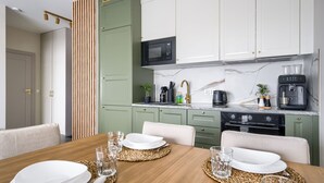 A modern kitchen with green cabinets, a microwave, a coffee maker, and a dining table set for four. - Apartamenty Sun & Snow Nad Odrą (Szczecin)