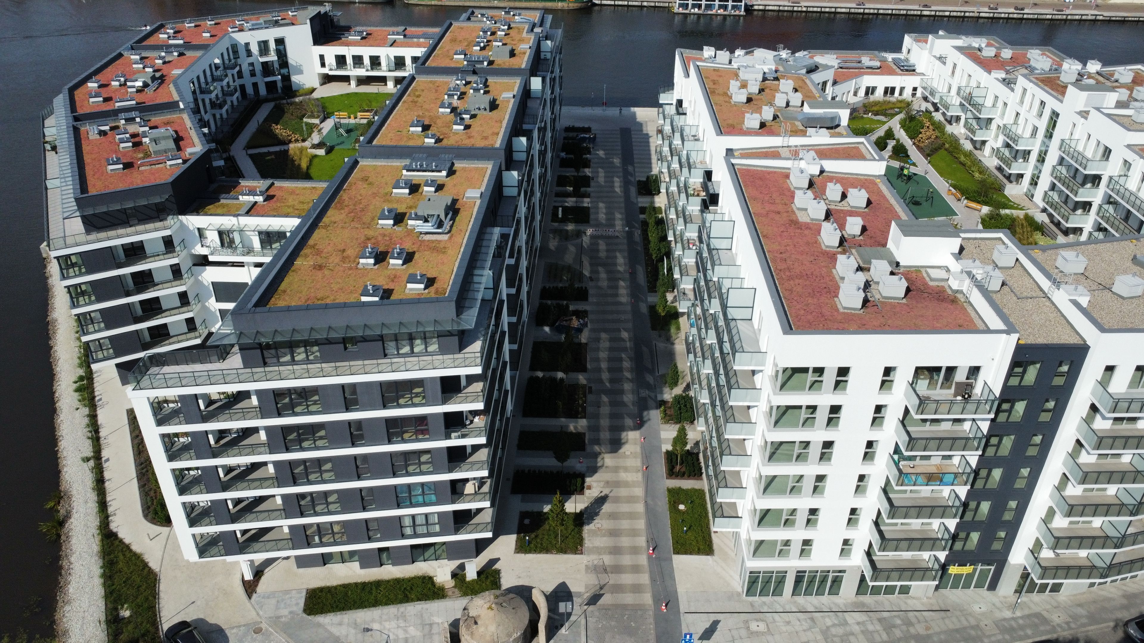 Un moderno complejo de apartamentos con varios edificios, terrazas en la azotea y un río al fondo.