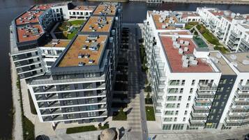 Un moderno complejo de apartamentos con varios edificios, terrazas en la azotea y un río al fondo.