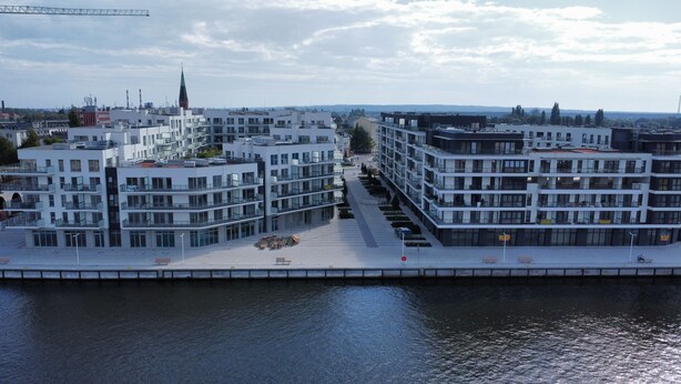 A modern urban area with multi-story buildings, a waterfront promenade, and a visible church spire in the background. - Apartamenty Sun & Snow Nad Odrą (Szczecin)