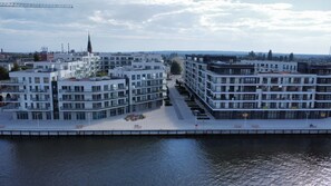 Un quartier urbain moderne avec des immeubles à plusieurs étages, une promenade en bord de mer et le clocher d’une église visible au loin.