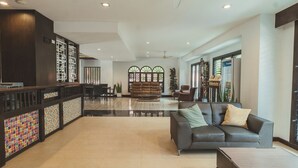 A spacious lobby with a grey sofa, a wooden reception desk, and a patterned wall. - Pink Residence Chalong (Rawai)