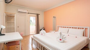 A hotel room with a bed, a desk, a chair, a wardrobe, and an air conditioning unit. - Pink Residence Chalong (Rawai)