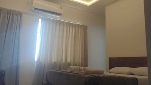 Une chambre d’hôtel avec un lit, une banquette, un appareil de climatisation et une fenêtre avec des rideaux.