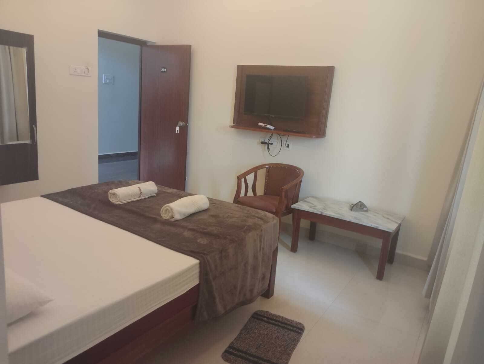 A hotel room with a bed, a chair, a small table, a TV, and a door.