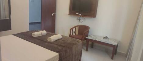 A hotel room with a bed, a chair, a small table, a TV, and a door.