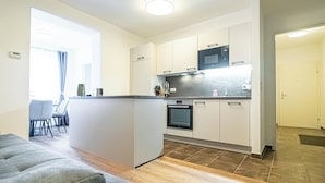 Una cocina moderna con armarios blancos, microondas y horno. Se ve un área de comedor con una mesa y sillas a través de un umbral.