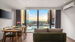 Uma sala de estar moderna com mesa de jantar de madeira, sofá verde e janelas amplas com vista para a cidade.