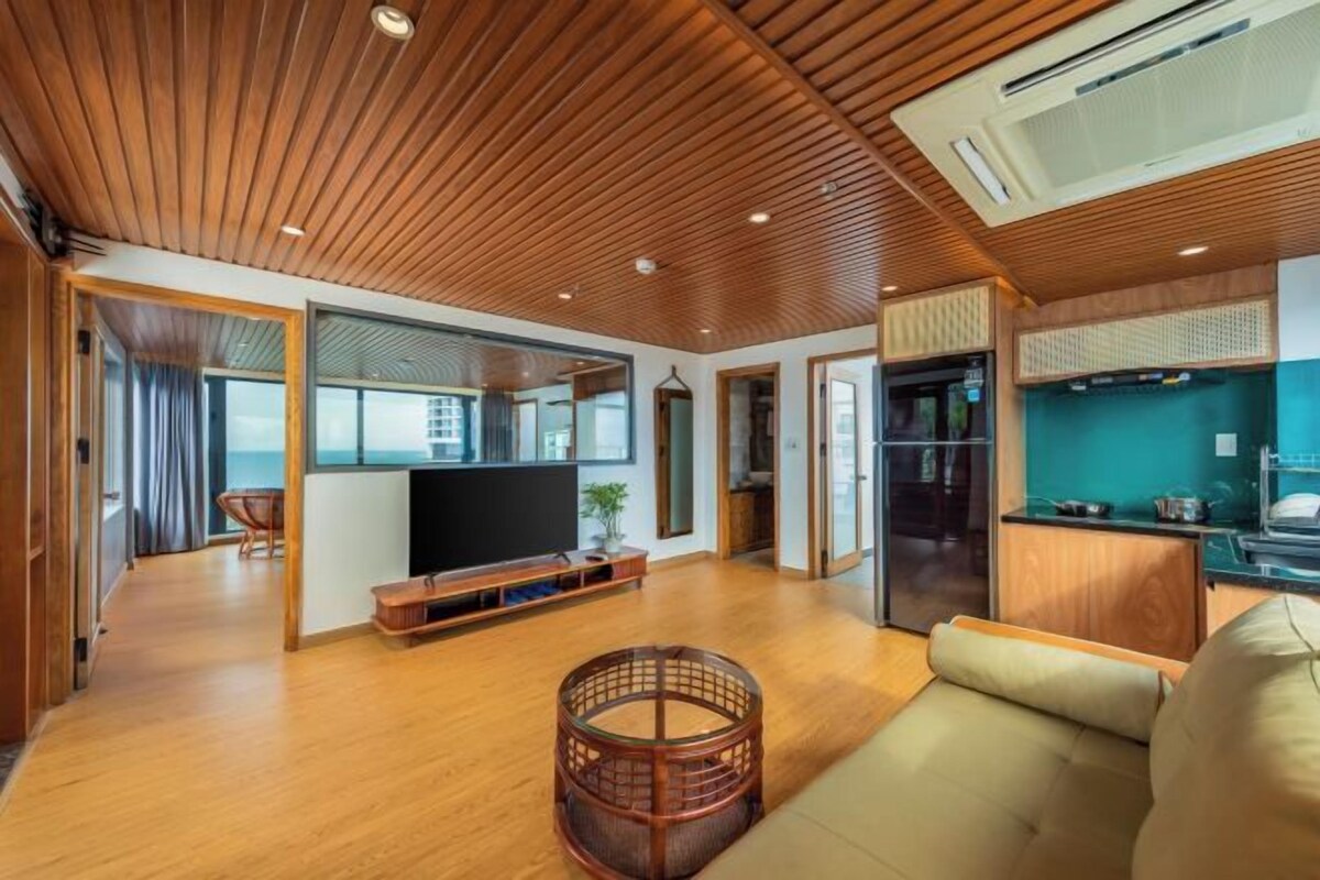 Ein modernes Wohnzimmer mit Holzböden, einem Fernseher, einem Sofa und einer Küchenzeile mit Kühlschrank und Herd.