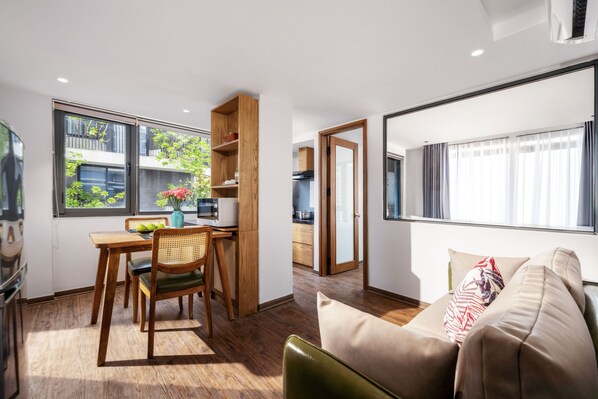 A modern living space with a dining area, a sofa, and a kitchen visible through an open door.