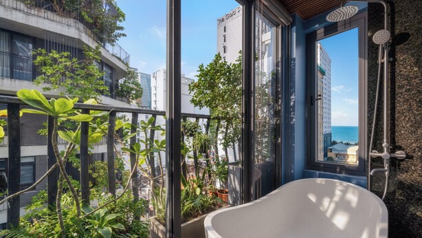 Uma casa de banho moderna com uma banheira independente, cabine de duche em vidro e vista para a cidade e o mar através de grandes janelas.