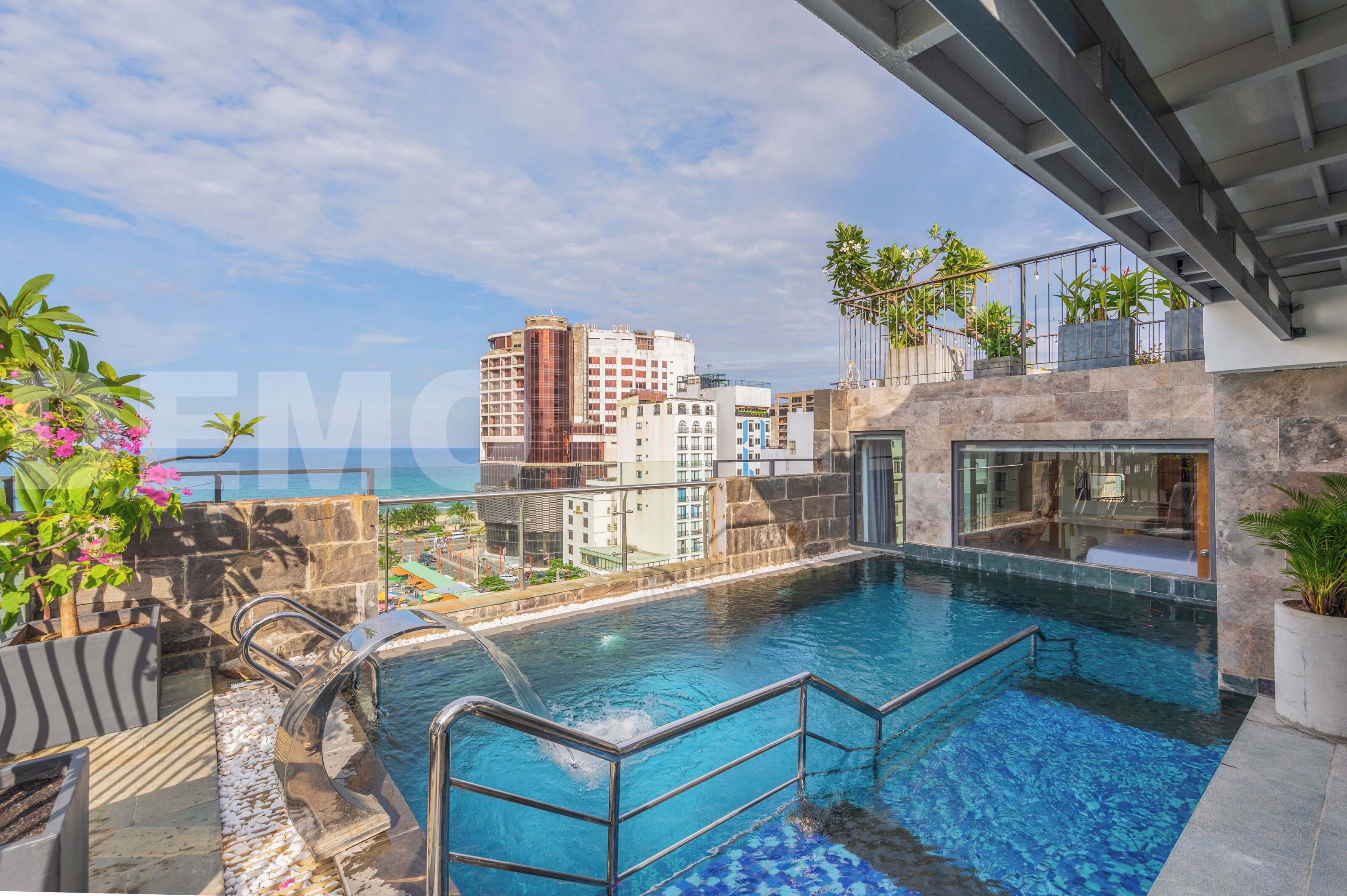 A rooftop pool with a view of the city skyline, stone walls, and potted plants.