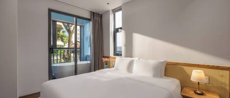 Habitación de hotel con una cama grande, una mesita de noche con lámpara, vistas al exterior y una ventana con cortinas.