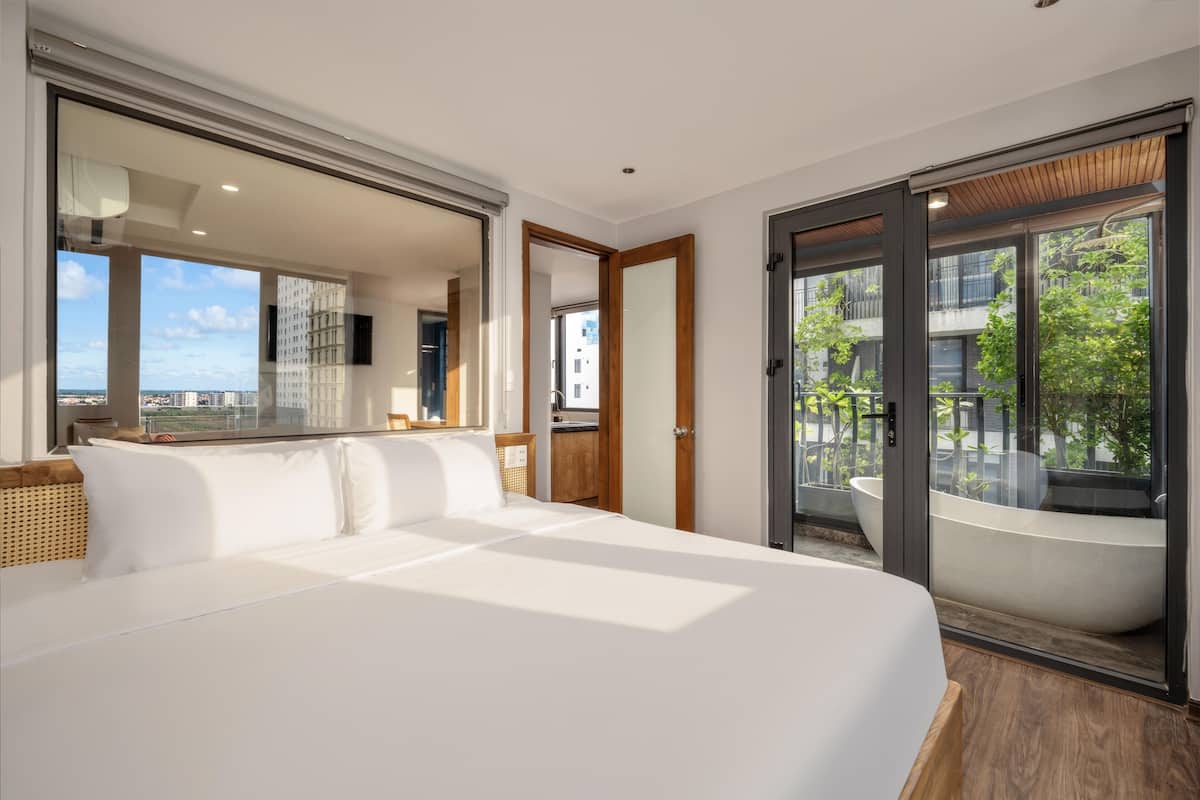 Een moderne hotelkamer met een groot bed, uitzicht op de stad en een eigen balkon met bad.