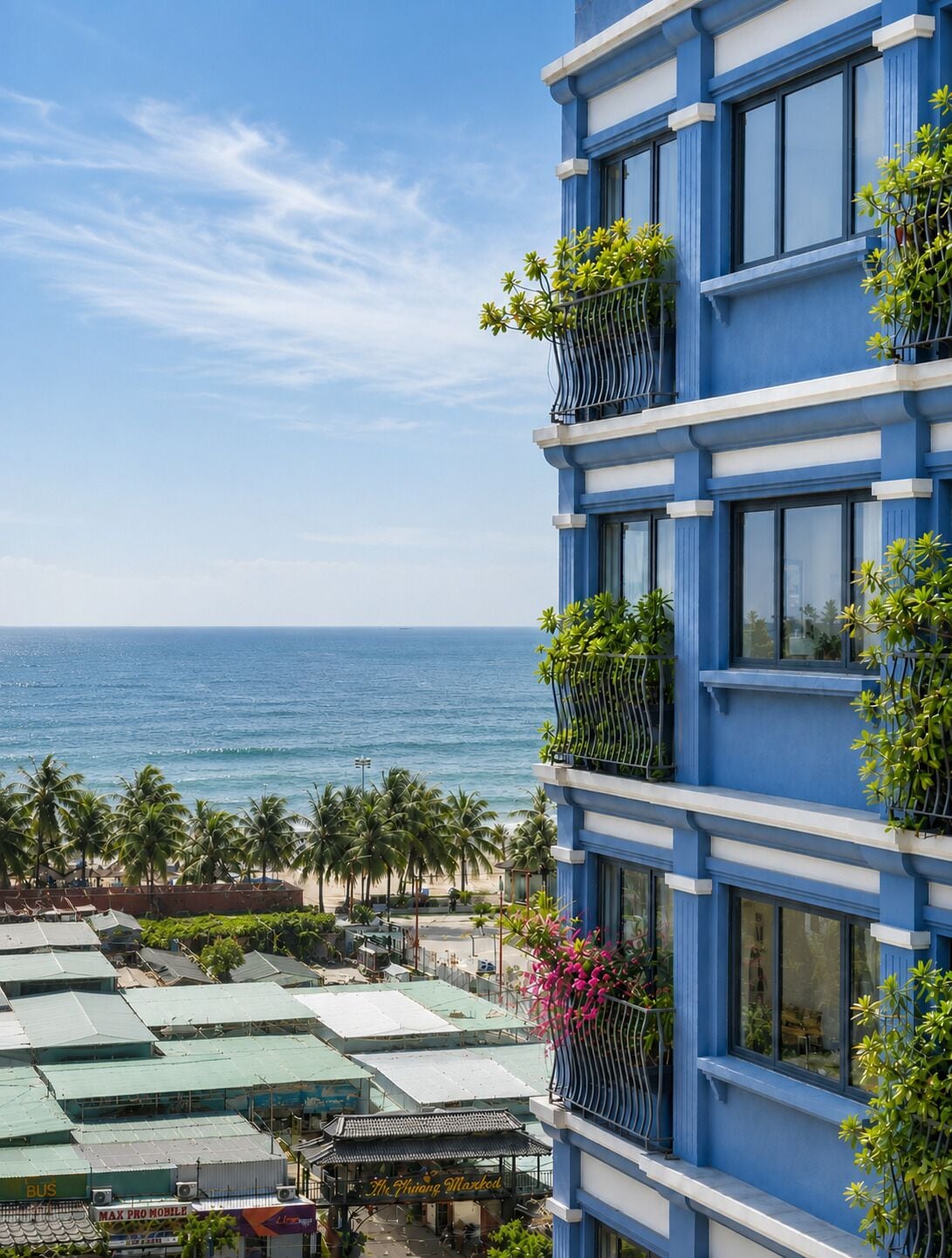 A multi-story building with balconies, a view of the ocean, and a beach with palm trees.