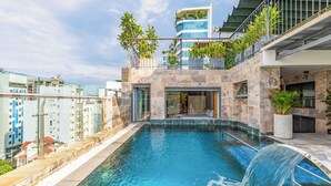 Piscina interior com cachoeira, rodeada por edifícios modernos e varandas com plantas.