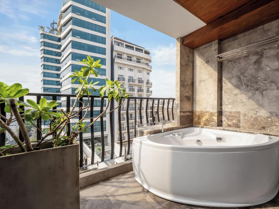 Une salle de bain moderne avec une baignoire sur pieds, un mur recouvert de pierres et un balcon agrémenté de plantes en pot.