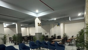 A spacious indoor area with a marble floor, blue chairs arranged in rows, and tables with chairs. - Hotel Divines Residency  (Noida)