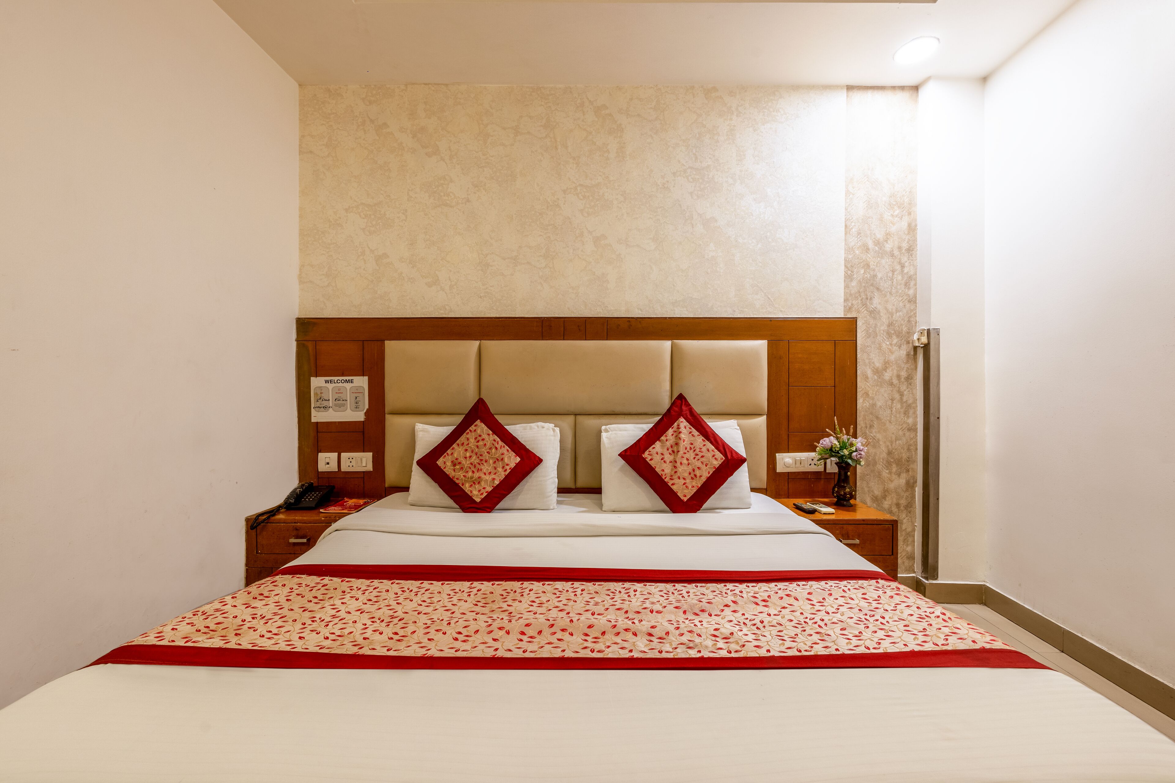 Een hotelkamer met een groot bed, een houten hoofdbord, twee nachtkastjes met lampen en een aan de muur bevestigde telefoon.
