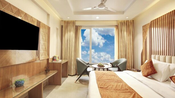A hotel room with a bed, a TV, a desk, a chair, and a window with a view of the sky. - Hotel Divines Residency  (Noida)