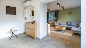 Een moderne woonkamer met een bank, salontafel en een kast. Er is een raam met gordijnen, een klok aan de muur en een plafondlamp.