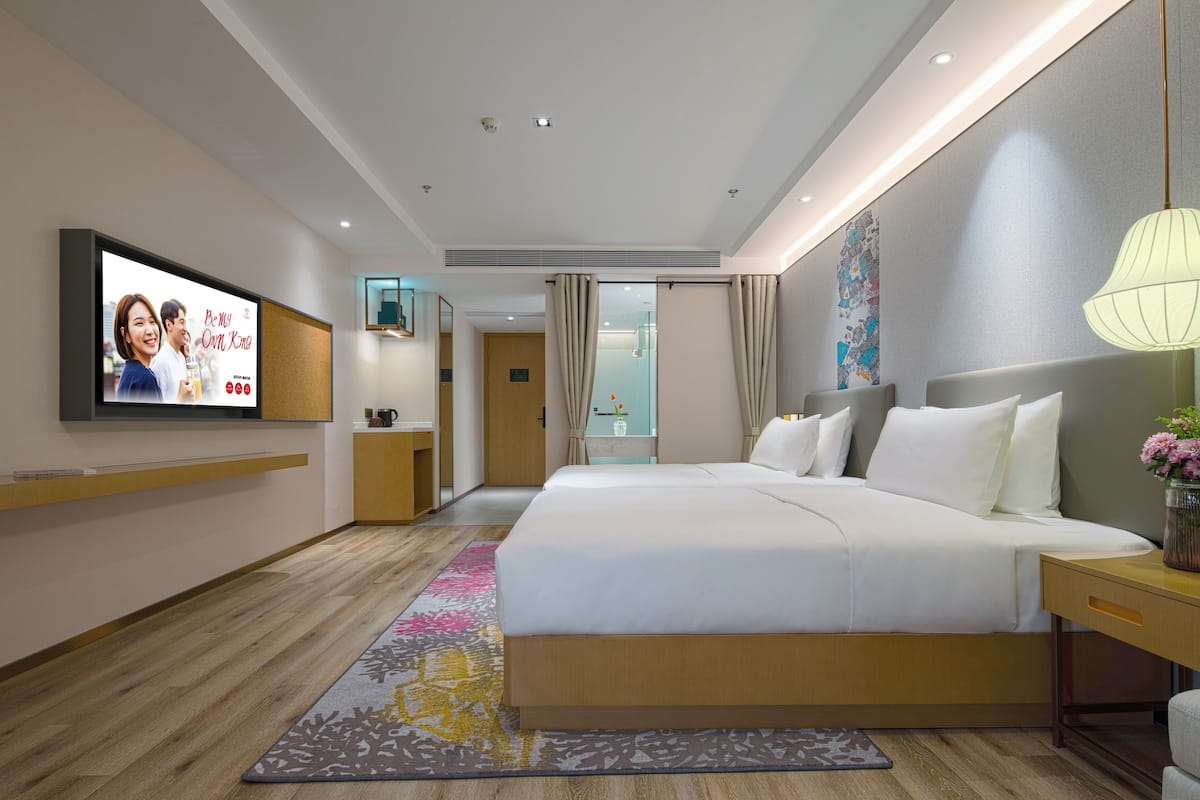 A modern hotel room with a large bed, bedside tables, a flat-screen TV, and a bathroom visible through a glass door.