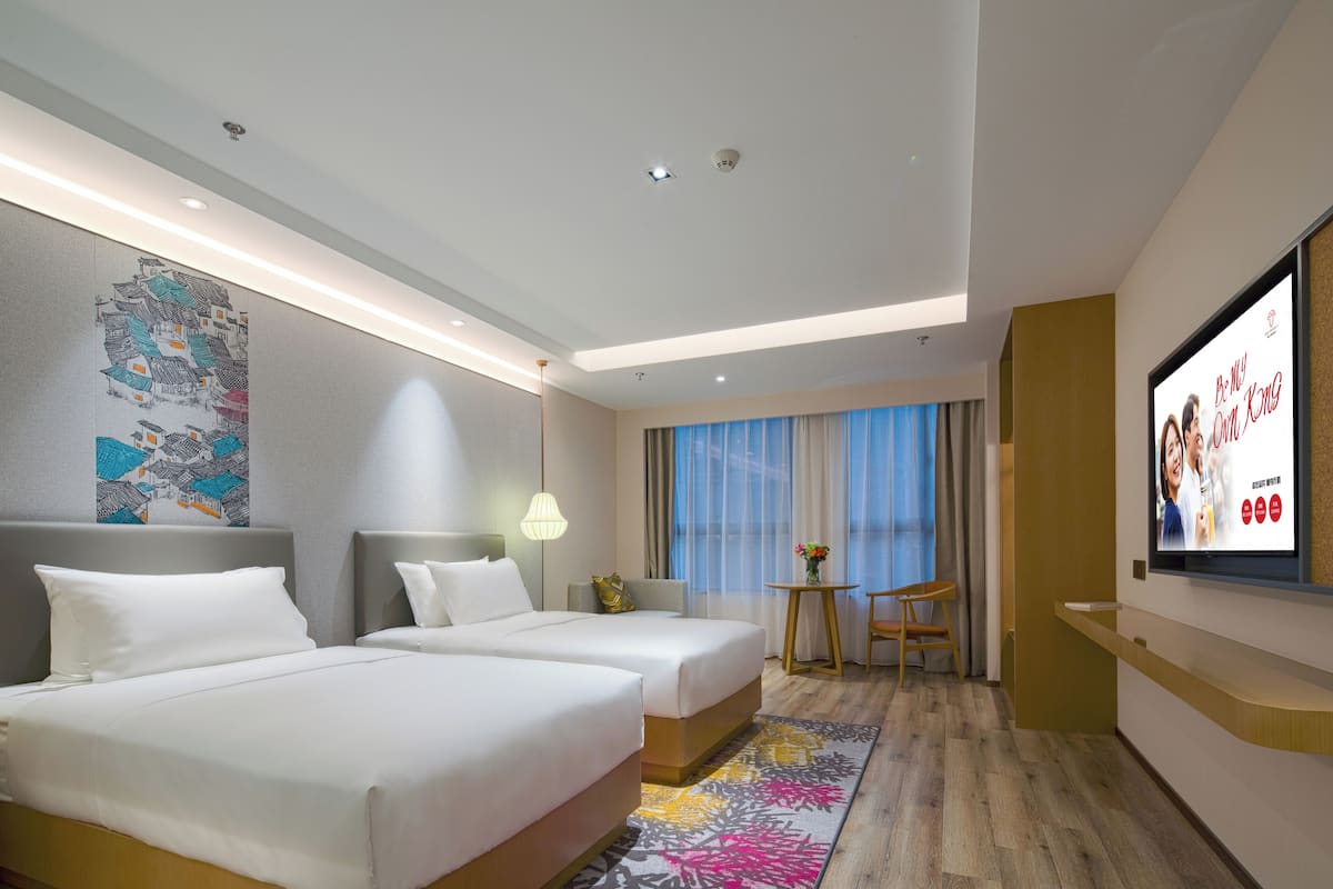 A hotel room with two beds, a TV, a desk, and a window with curtains.