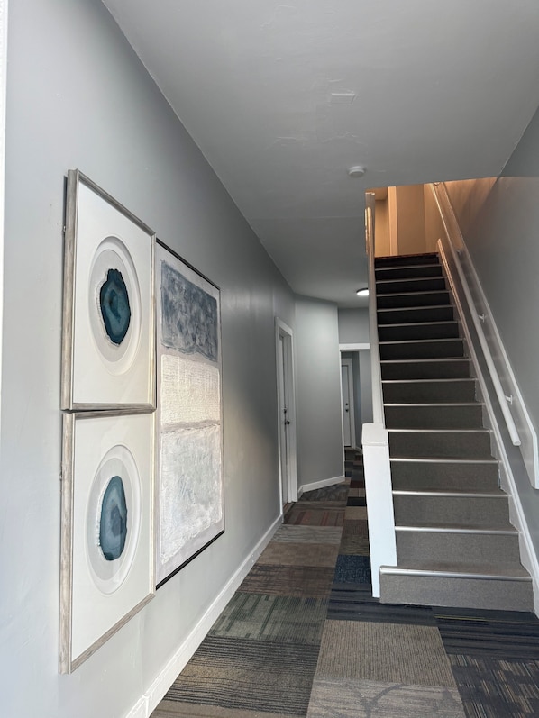 A hallway with a staircase, a patterned carpet, and framed artwork on the walls.