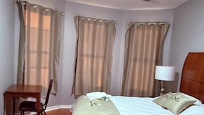 Una habitación de hotel con cama, escritorio, silla, lámpara y cortinas.