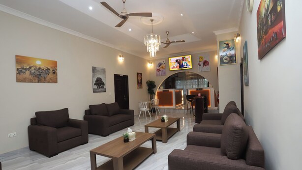A modern living room with sofas, a coffee table, and a TV. There are ceiling fans, a chandelier, and artwork on the walls. - Wepia Guest House (Oyibi)
