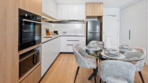 Une cuisine moderne dotée d’appareils électroménagers intégrés, d’une table à manger avec des chaises et de meubles de rangement blancs.