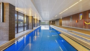 Piscina interior com paredes de vidro transparente, painéis de madeira e vista para o exterior.