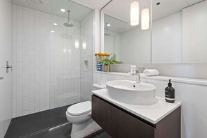 Een moderne badkamer met een wit wastafeltje, een donker aanrechtblad en een grote spiegel.