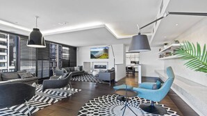 Uma sala de estar moderna com um sofá, poltronas, uma mesa de centro e uma televisão. Há tapetes com padrão preto e branco no chão.