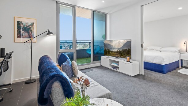Quarto de hotel moderno com uma janela grande, uma cama, uma TV e um sofá.