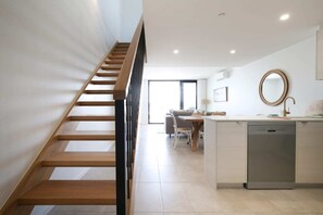 Eine moderne Küche mit einer Holztreppe, einem Essbereich und Blick ins Freie.