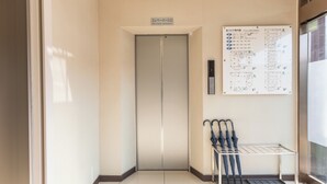 Ein sauberes, modernes Aufzug-Entree mit einem Grundriss-Schild und einem Metallgestell für Regenschirme.