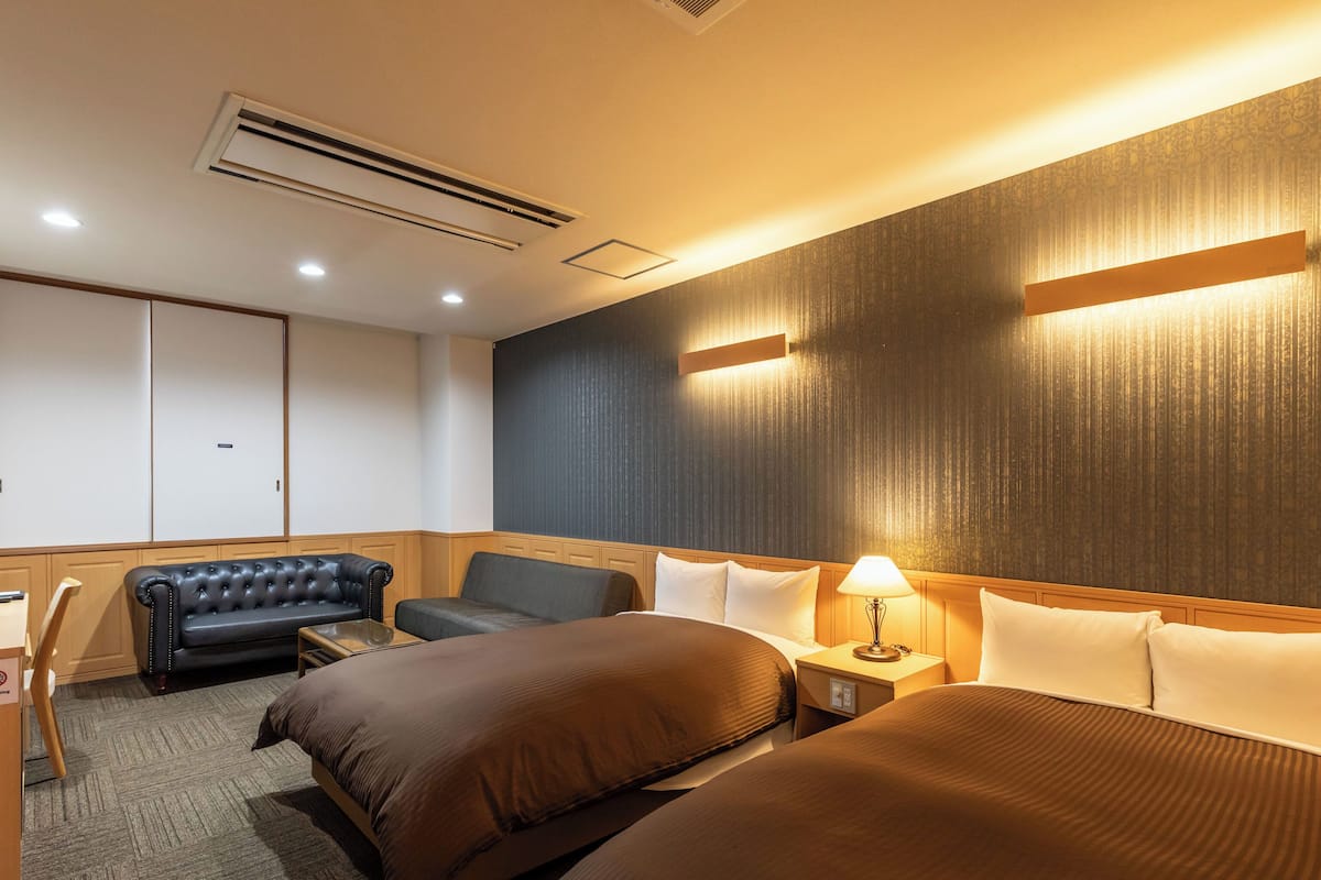 A hotel room with two beds, a sofa, a desk, and a wardrobe.