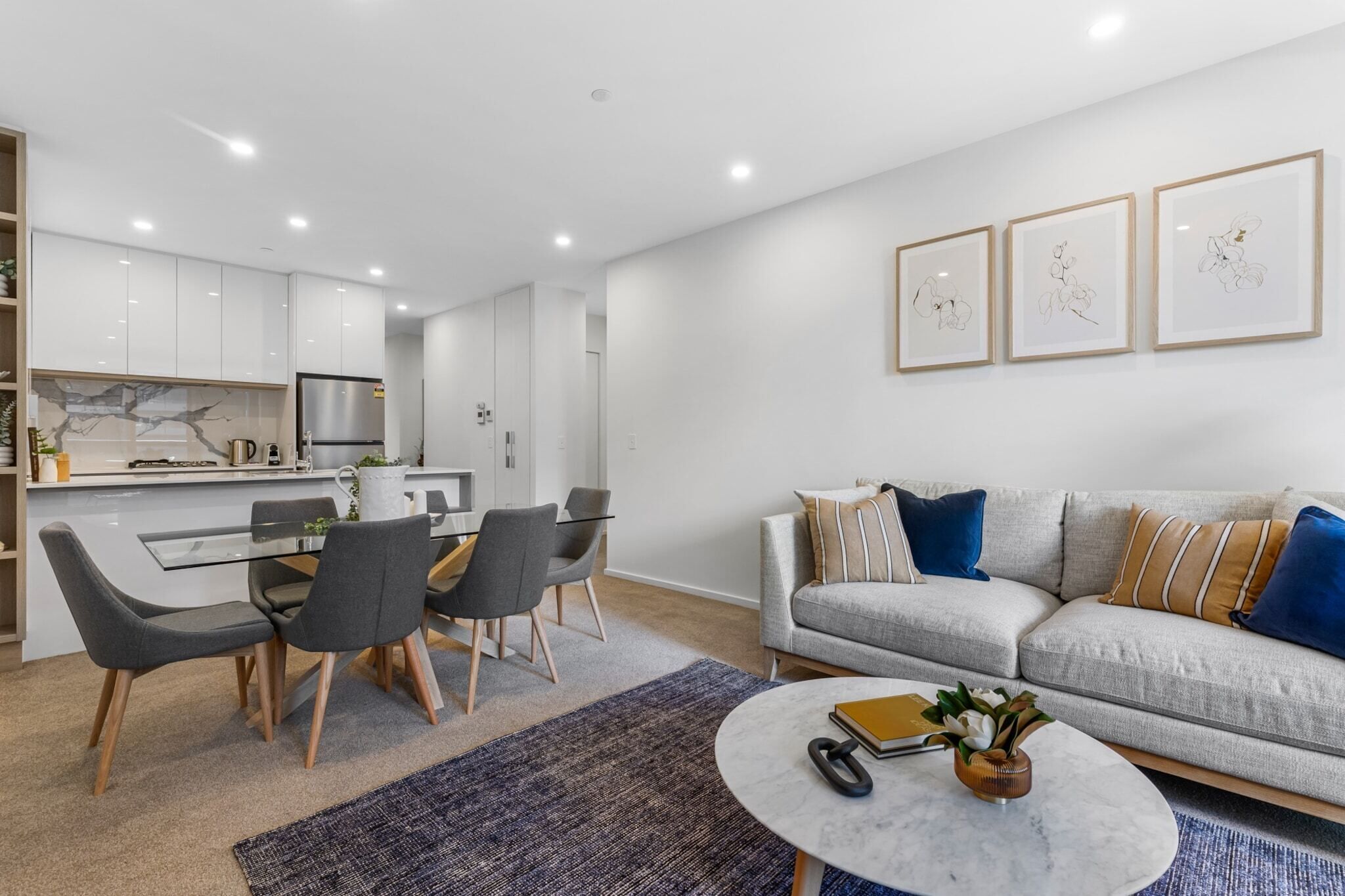 A modern living room with a grey sofa, a coffee table, and a dining area with a glass table and chairs.
