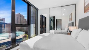 Una habitación de hotel moderna con ventanas amplias, una cama, un escritorio y un espejo.